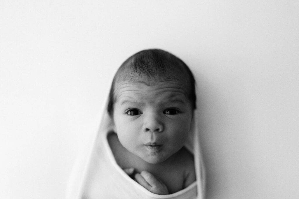 Newborn-kuvaus Helsinki - vastasyntynyt vauva katsoo silmä suurina kameraan mustavalkokuvassa