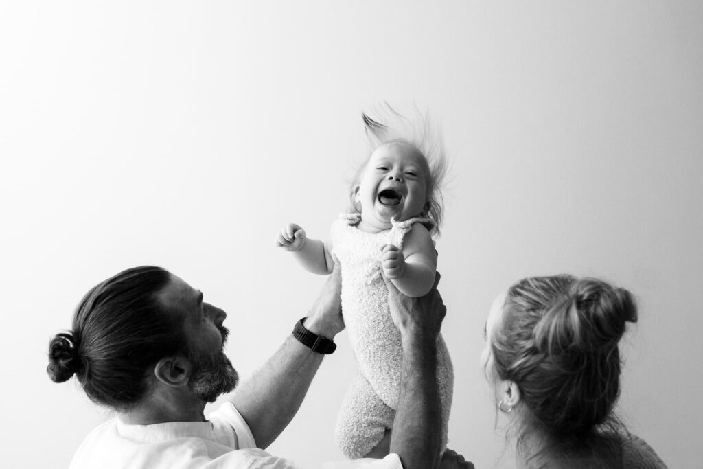 Perhekuvaus Helsinki - 1-vuotias lapsi nauraa mustavalkoisessa kuvassa isän nostaessa hänet ilmaan.